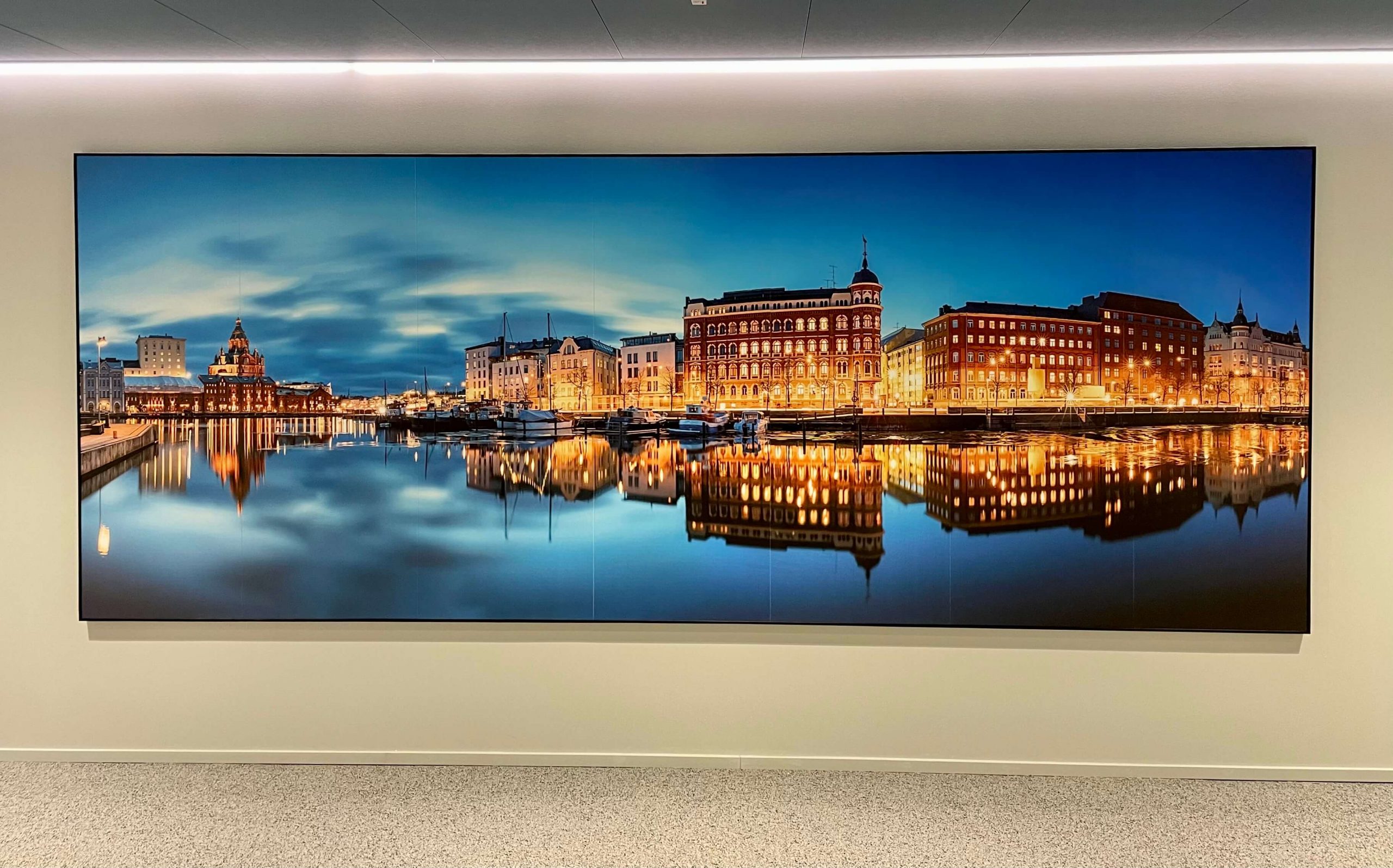 Toimitilan käytävän seinälle on ripustettu suuri taulu, jossa ilta-aikaan veden päältä kuvattu Helsingin-maisema jatkuu akustiikkalevyiltä toisille.